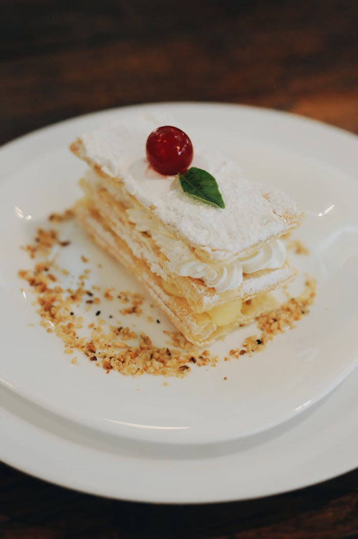 Home Indulge in a creamy layered pastry topped with a cherry and garnished with nuts.