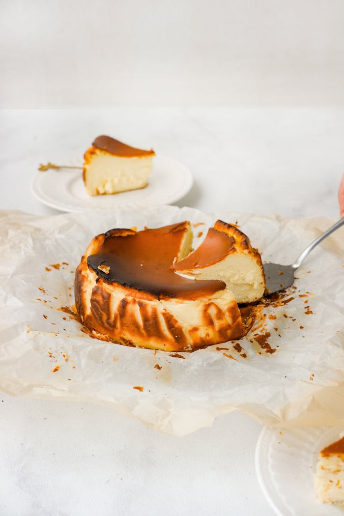 Home A creamy Basque burnt cheesecake with a slice served on a plate, showcasing its rich and indulgent texture.